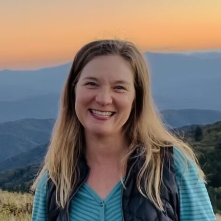 Closeup of ADC Project Manager Julie Judkins grinning in front of a sunset over mountains.